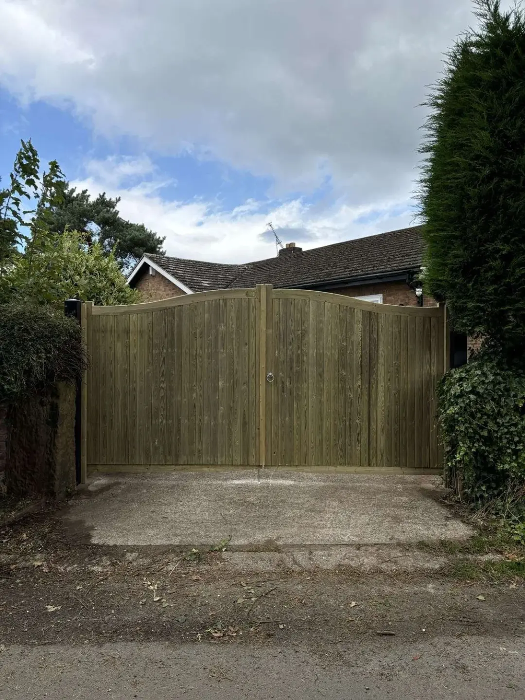 Pair of arched timber driveway gates closed across a drive